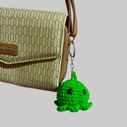 Green crocheted octopus keychain attached to a beige handbag on a pink fabric background