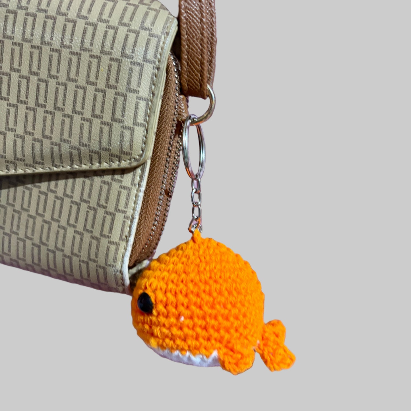 Small orange crocheted whale keychain attached to a beige handbag on a pink fabric background