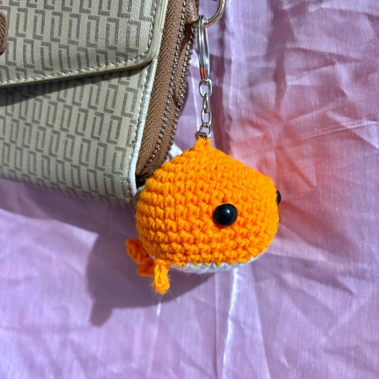 Crocheted whale keychain attached to a bag on a textured surface
