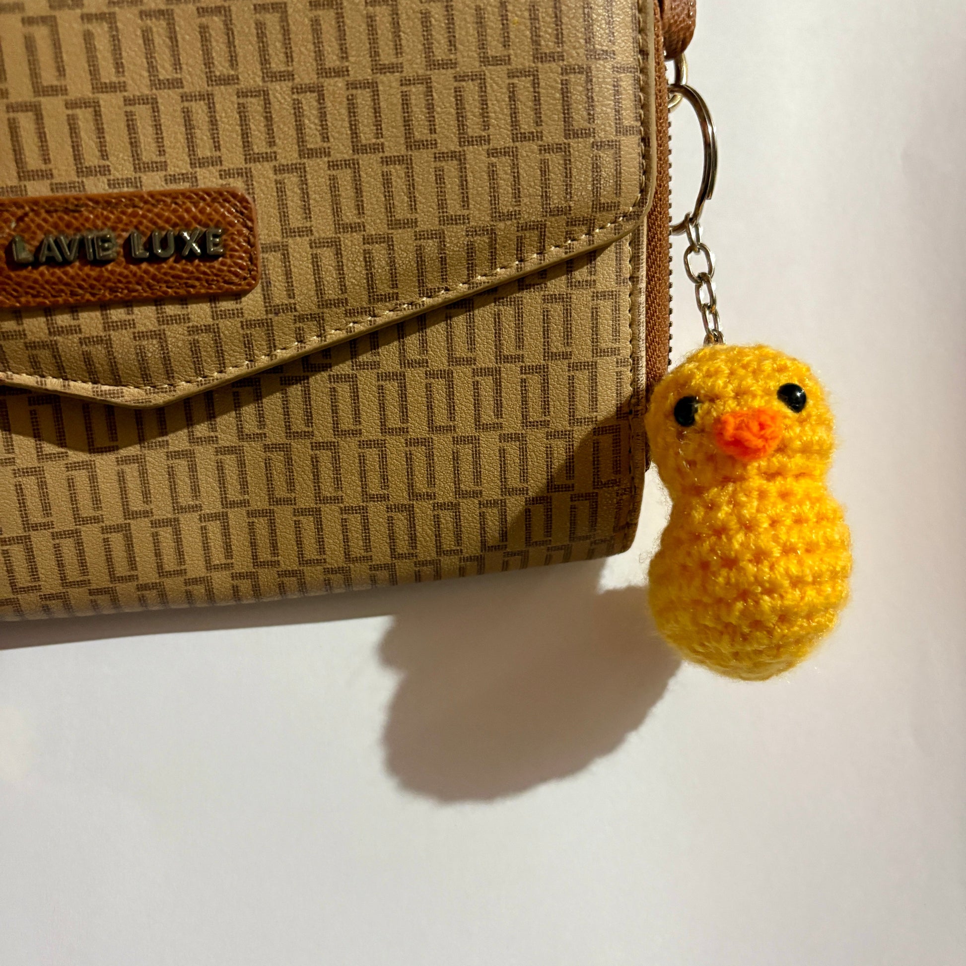 Yellow duck keychain attached to a brown patterned handbag on a white surface