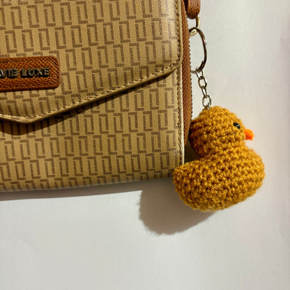Beige patterned handbag with a yellow crocheted duck keychain on a white background