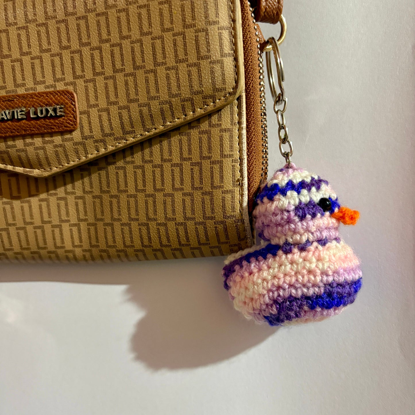 Crocheted duck keychain attached to a beige handbag on a light background