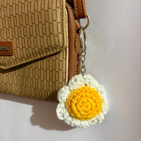 Brown textured handbag with a yellow and white crocheted flower keychain on a light gray background