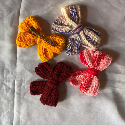 Colorful crocheted bow hair clips on a white fabric background