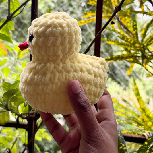 Hand holding a yellow crochet duck toy with a blurred green outdoor background