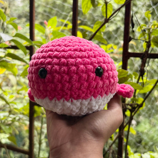 Crocheted pink and white whale held in a hand with a blurred green background