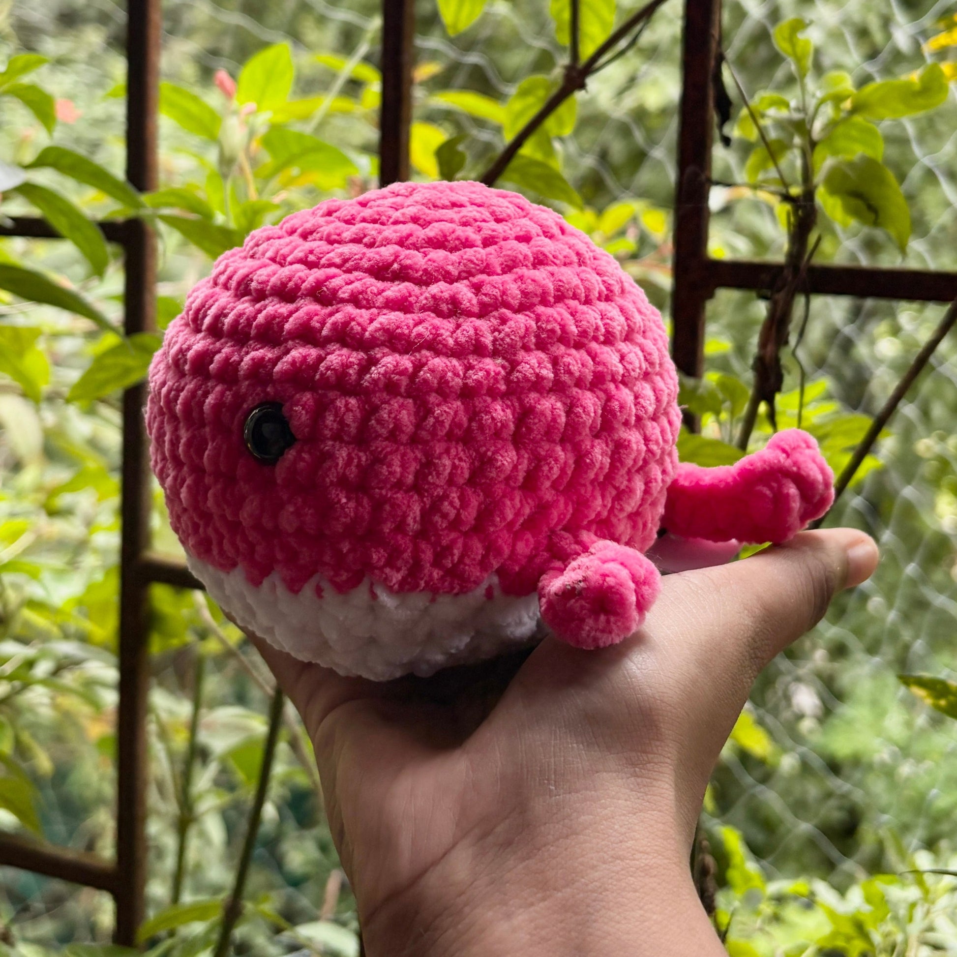 Hand holding a pink crochet whale against a natural background