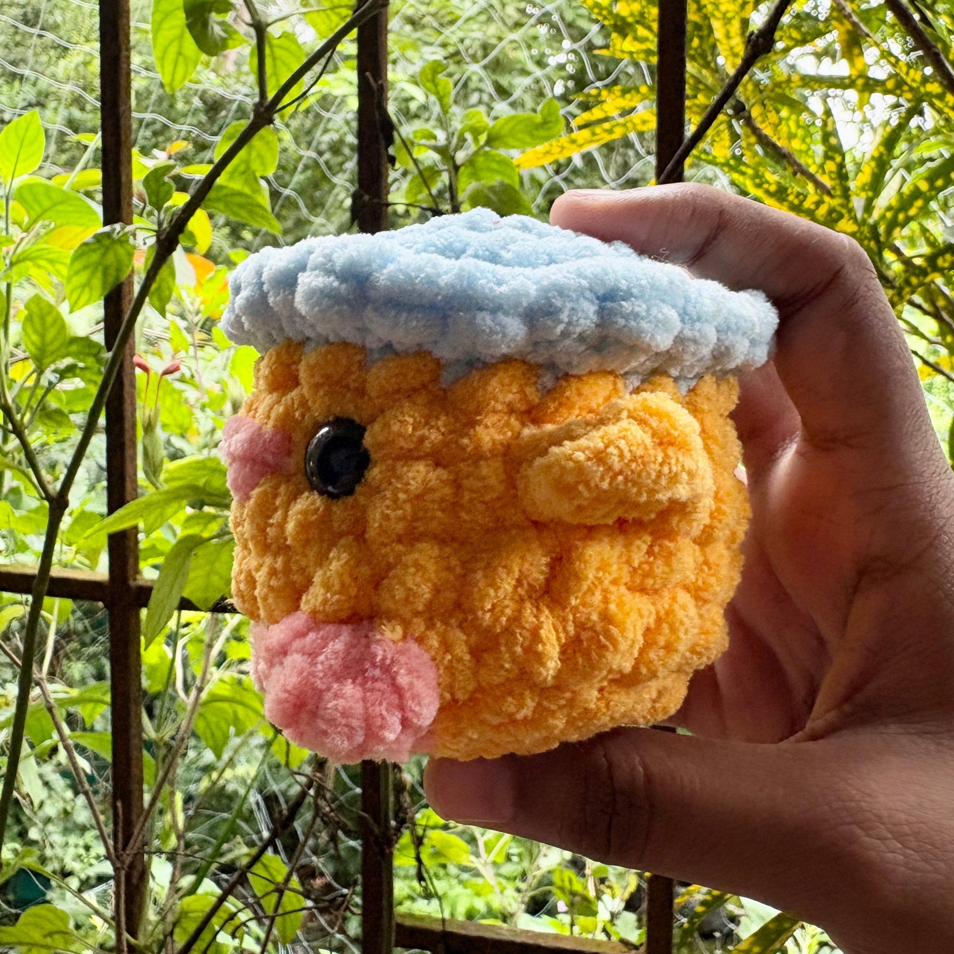 Hand holding a small plush toy resembling a hamster with a green outdoor background
