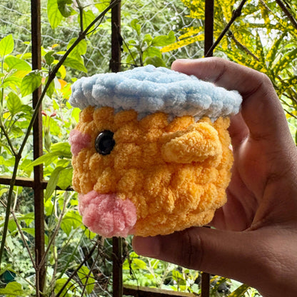 Hand holding a small plush toy resembling a hamster with a green outdoor background