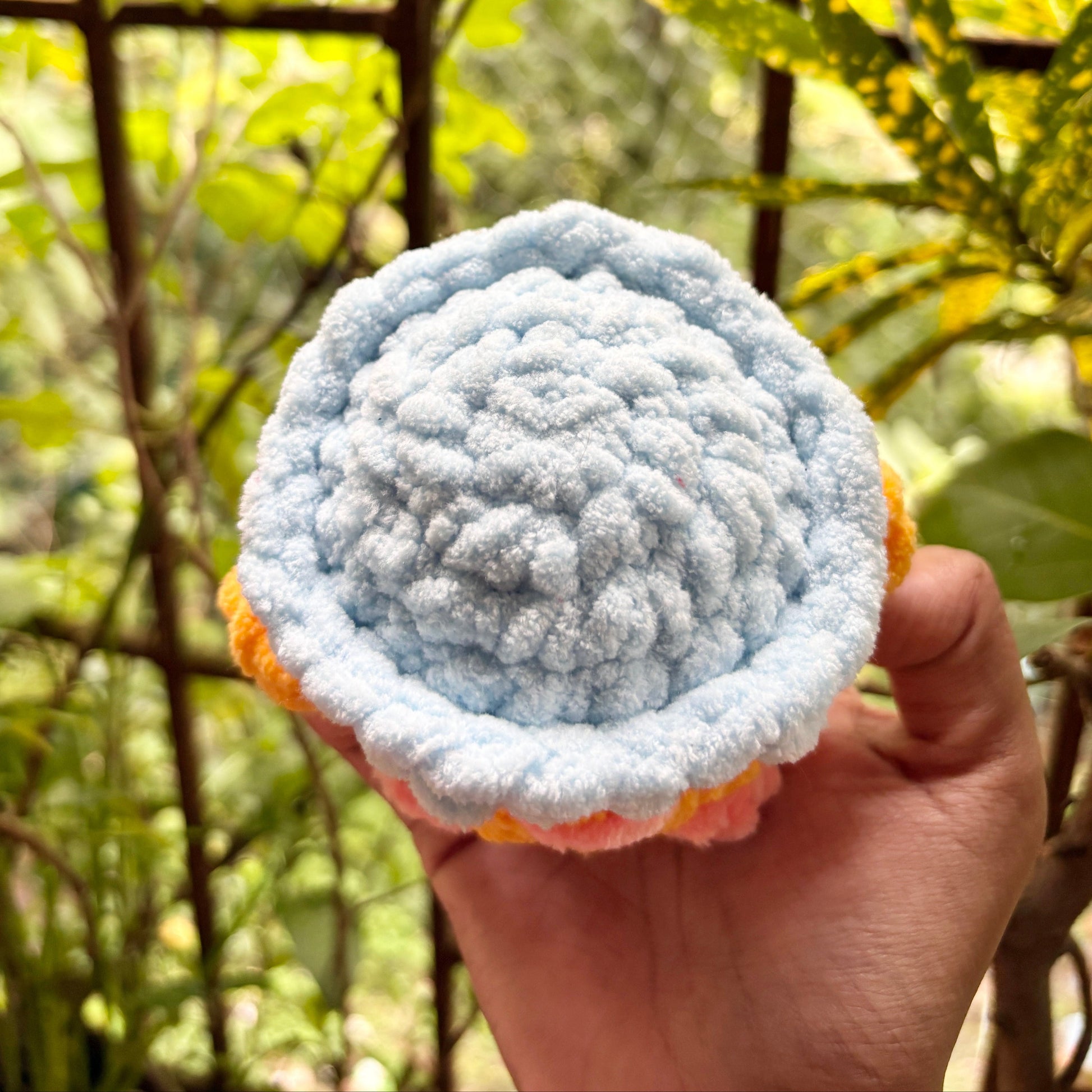Hand holding a textured blue and orange ball against a natural background