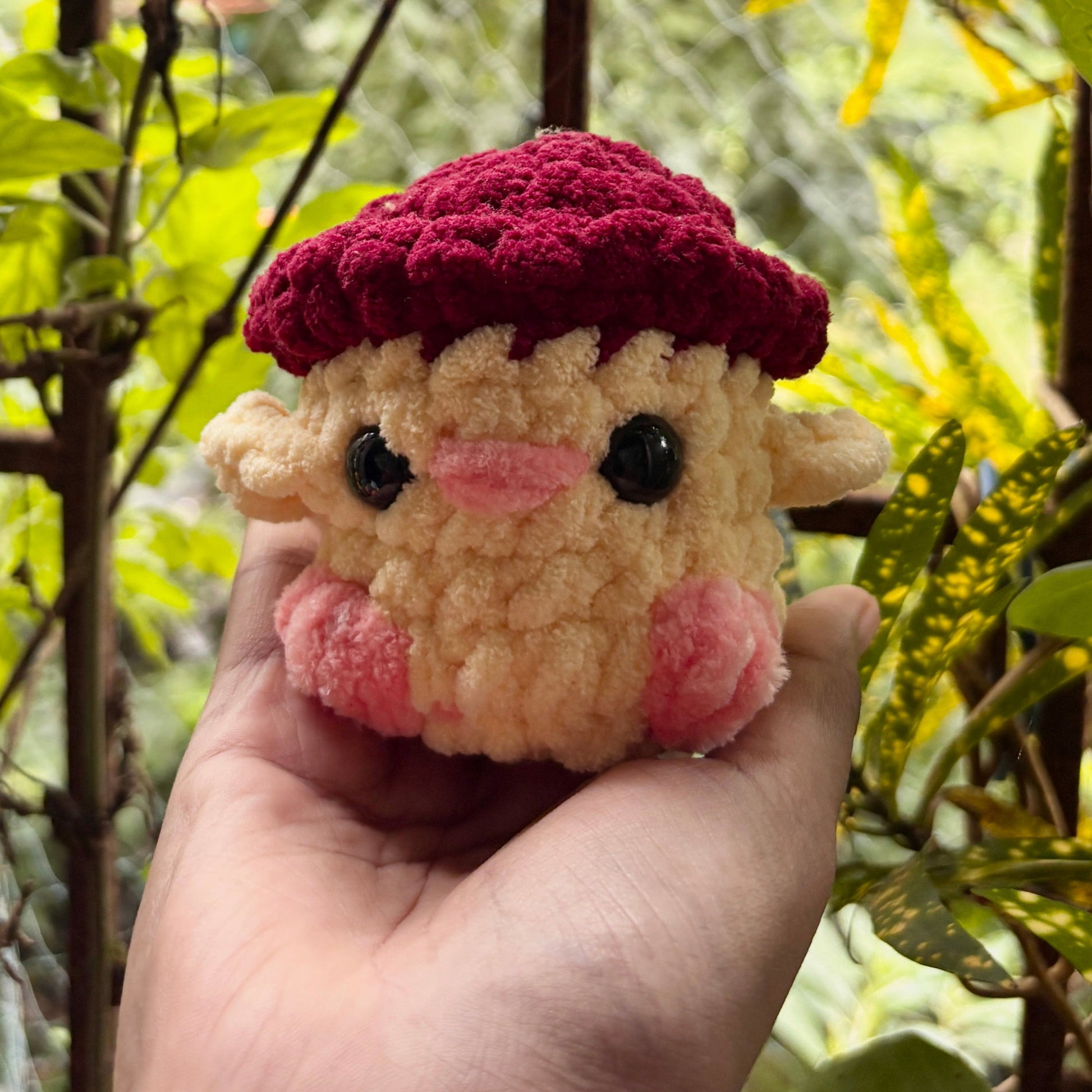 Small plush toy with a red hat held in a hand against a natural background