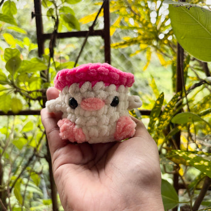 Hand holding a small crochet sheep toy with a pink hat against a natural background