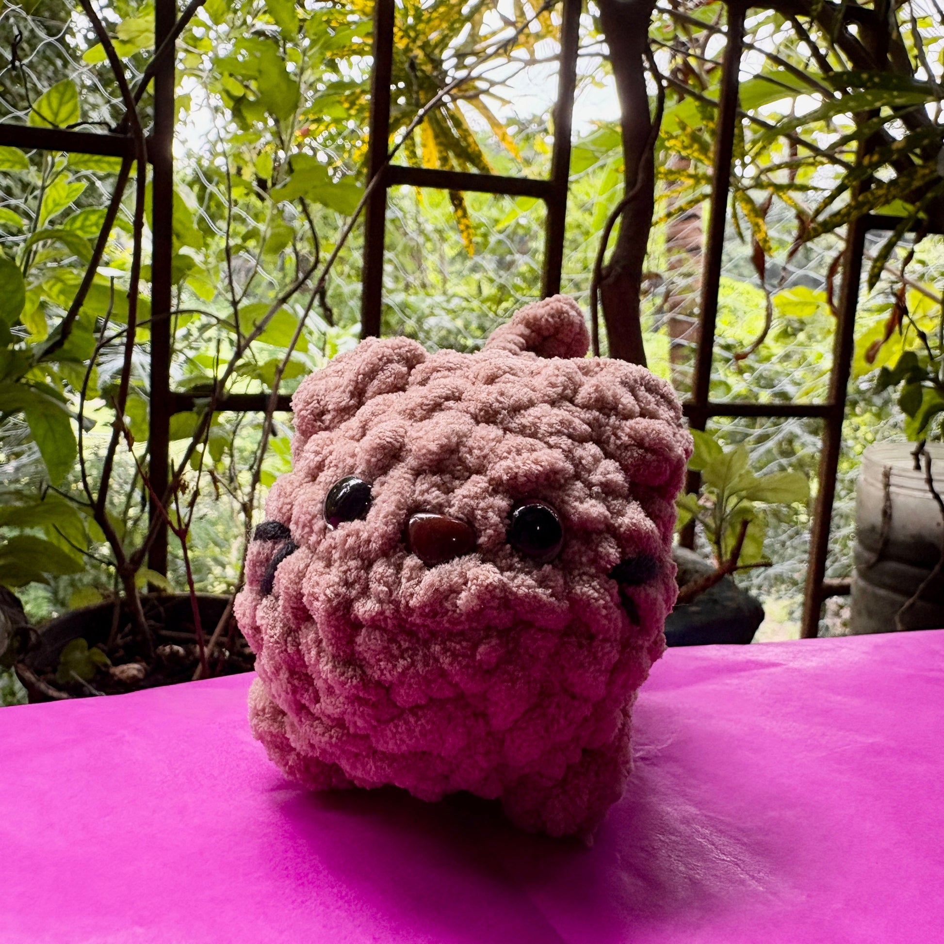 Pink plush bulldog toy on a pink surface with a garden background