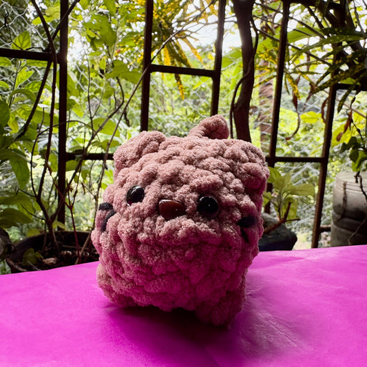Pink plush bulldog toy on a pink surface with a garden background