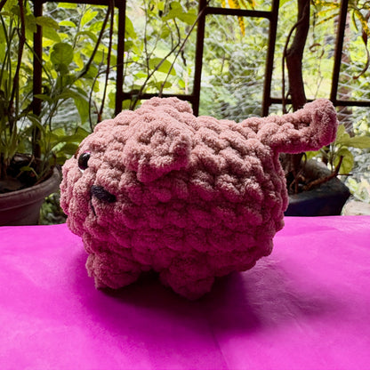 Pink knitted toy on a pink surface with a garden background