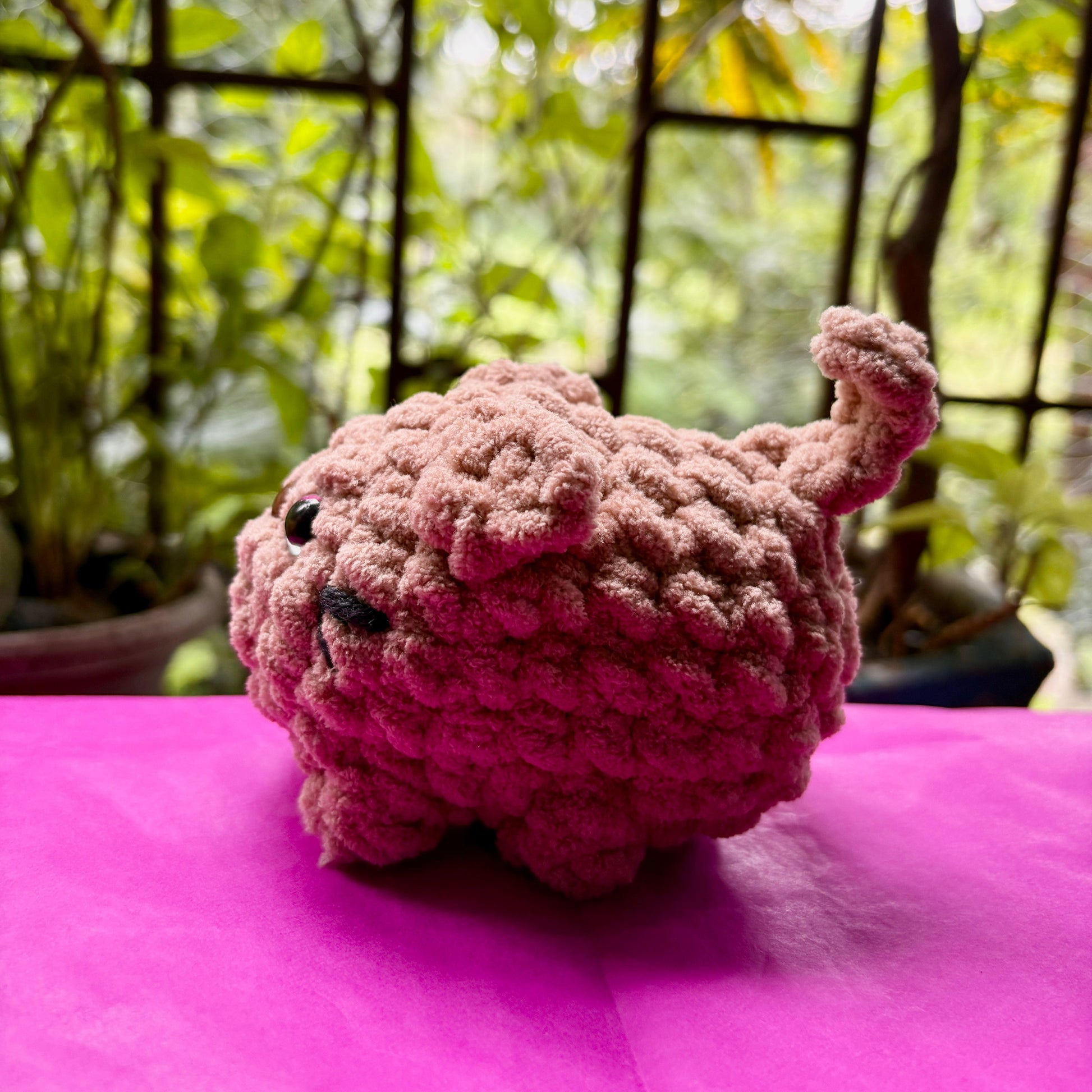 Pink knitted toy on a pink surface with a blurred green outdoor background