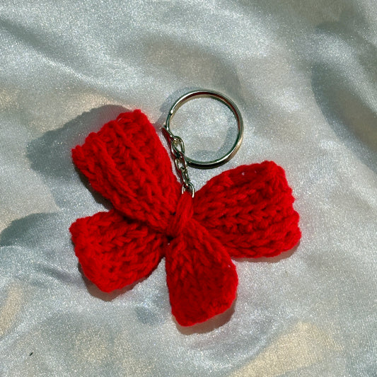 Red crochet bow keychain on a silver fabric background