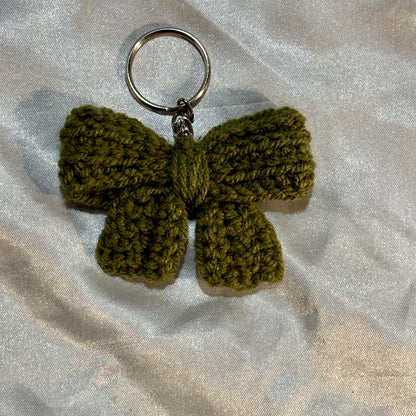 Green crocheted bow keychain on a light gray fabric background