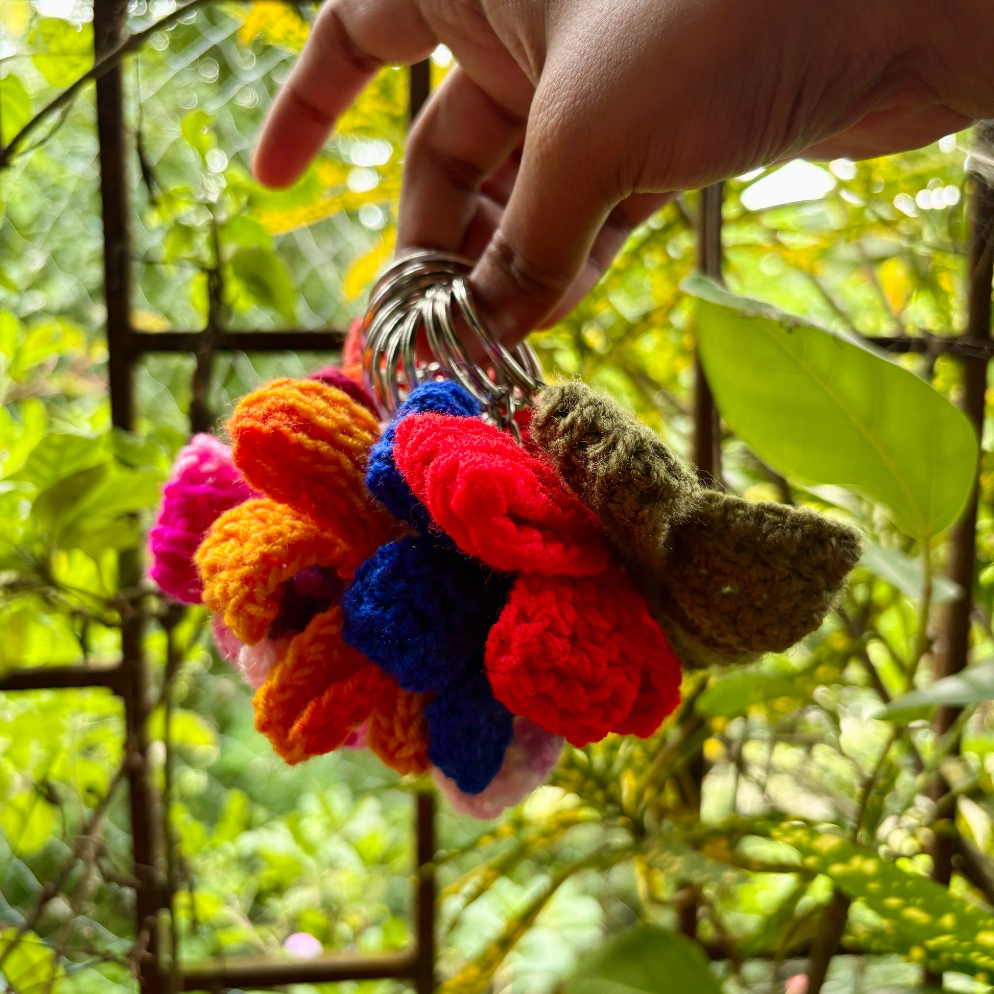 Colorful crocheted bow keychain held by a hand with a blurred green background