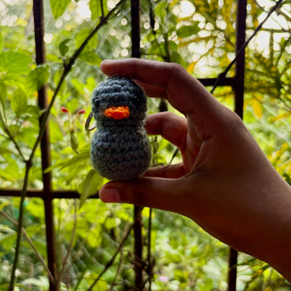 Hand holding a small crocheted duck toy in front of a blurred natural background