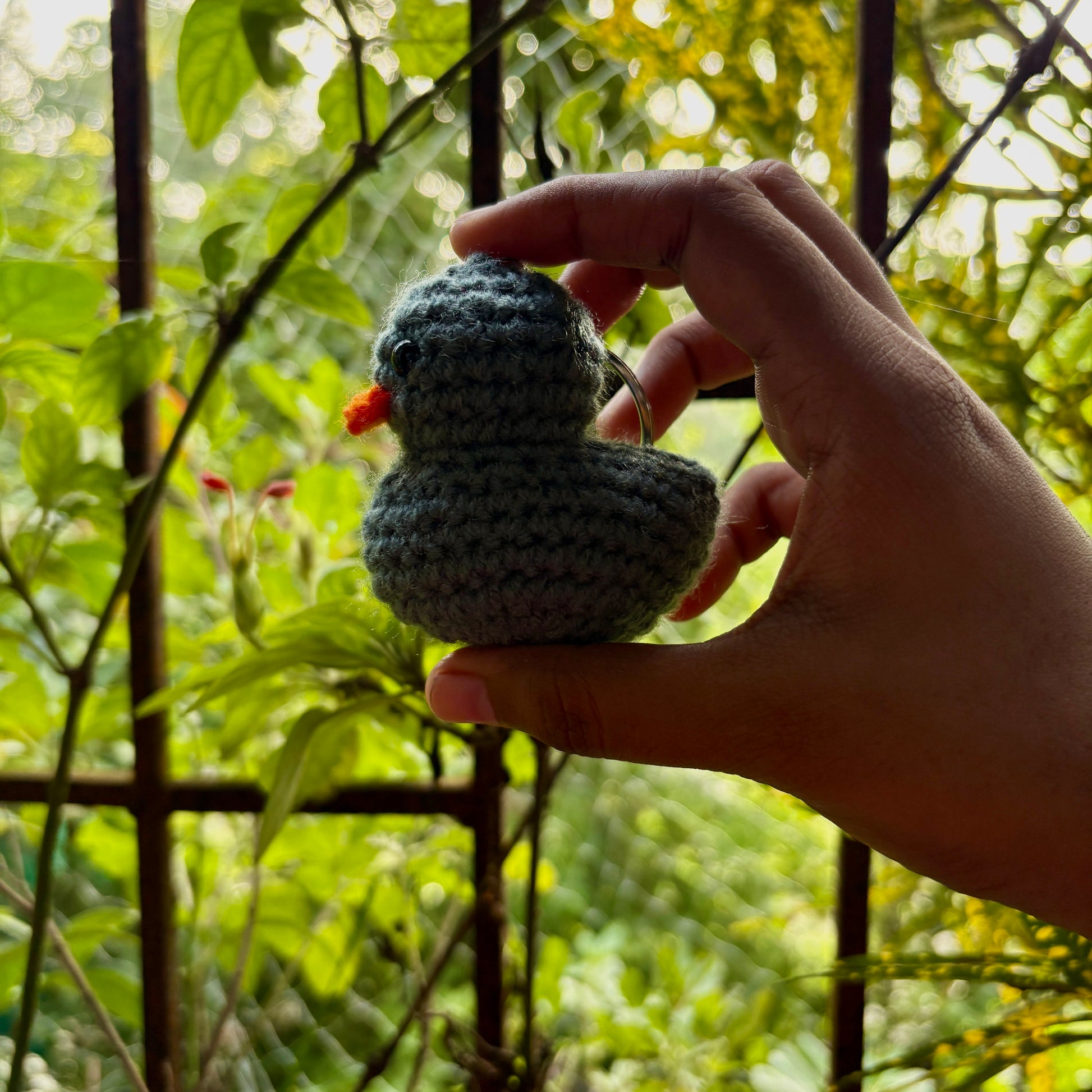 Hand holding a small crocheted bird against a natural background