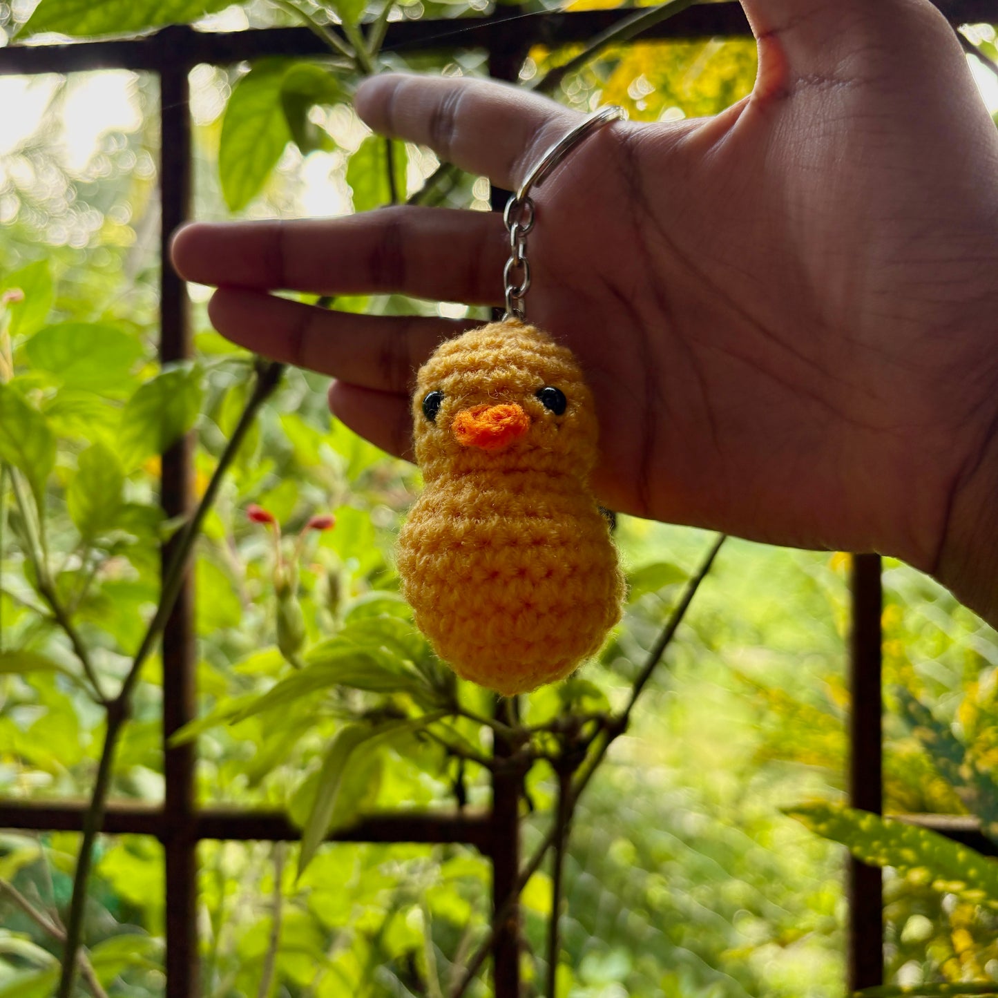 Hand holding a small yellow crocheted duck keychain with a green leafy background