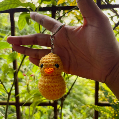 Hand holding a yellow crocheted duck keychain with a blurred green background