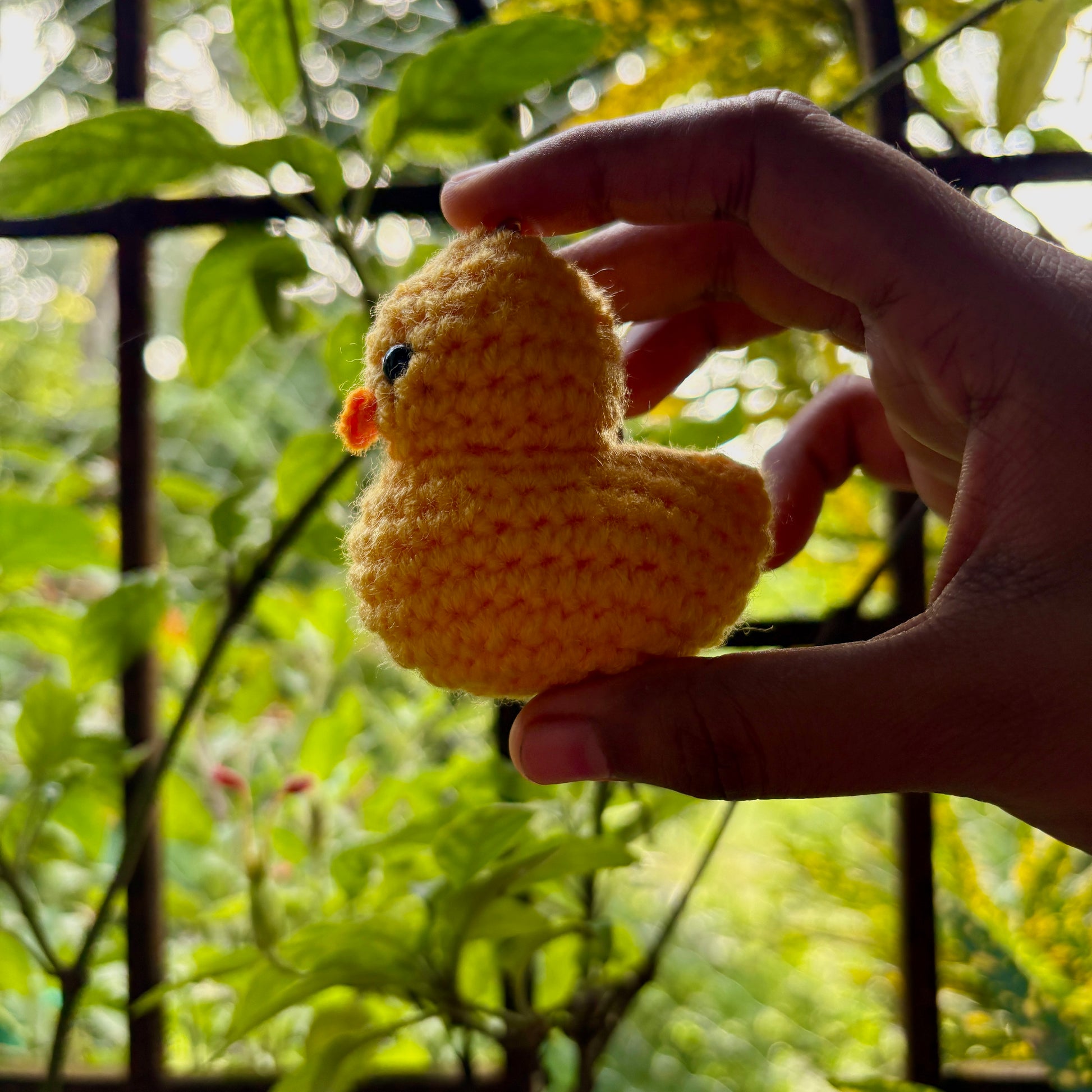 Hand holding a small yellow crocheted duck toy with a blurred green background