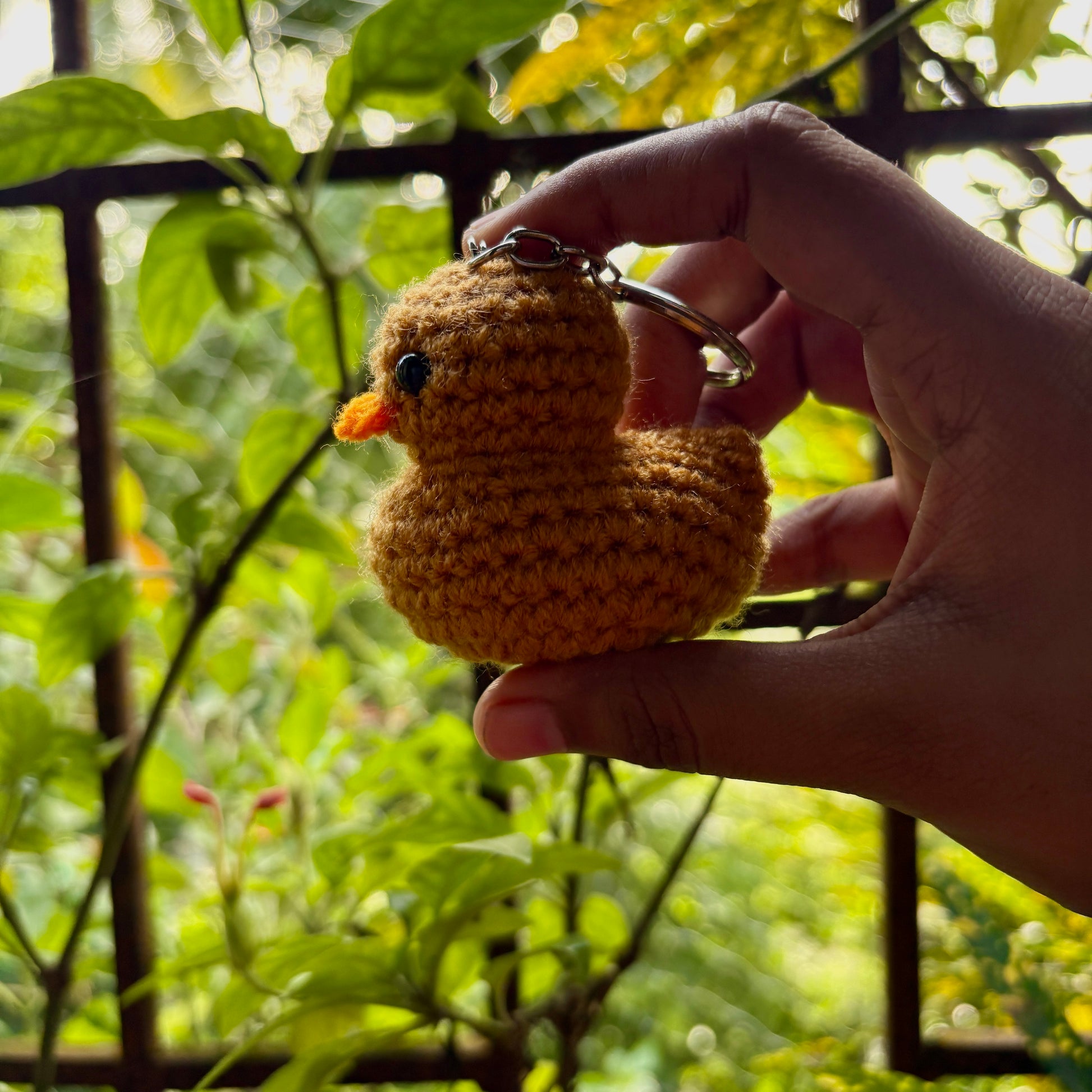Hand holding a small crocheted duck keychain with a green, leafy background