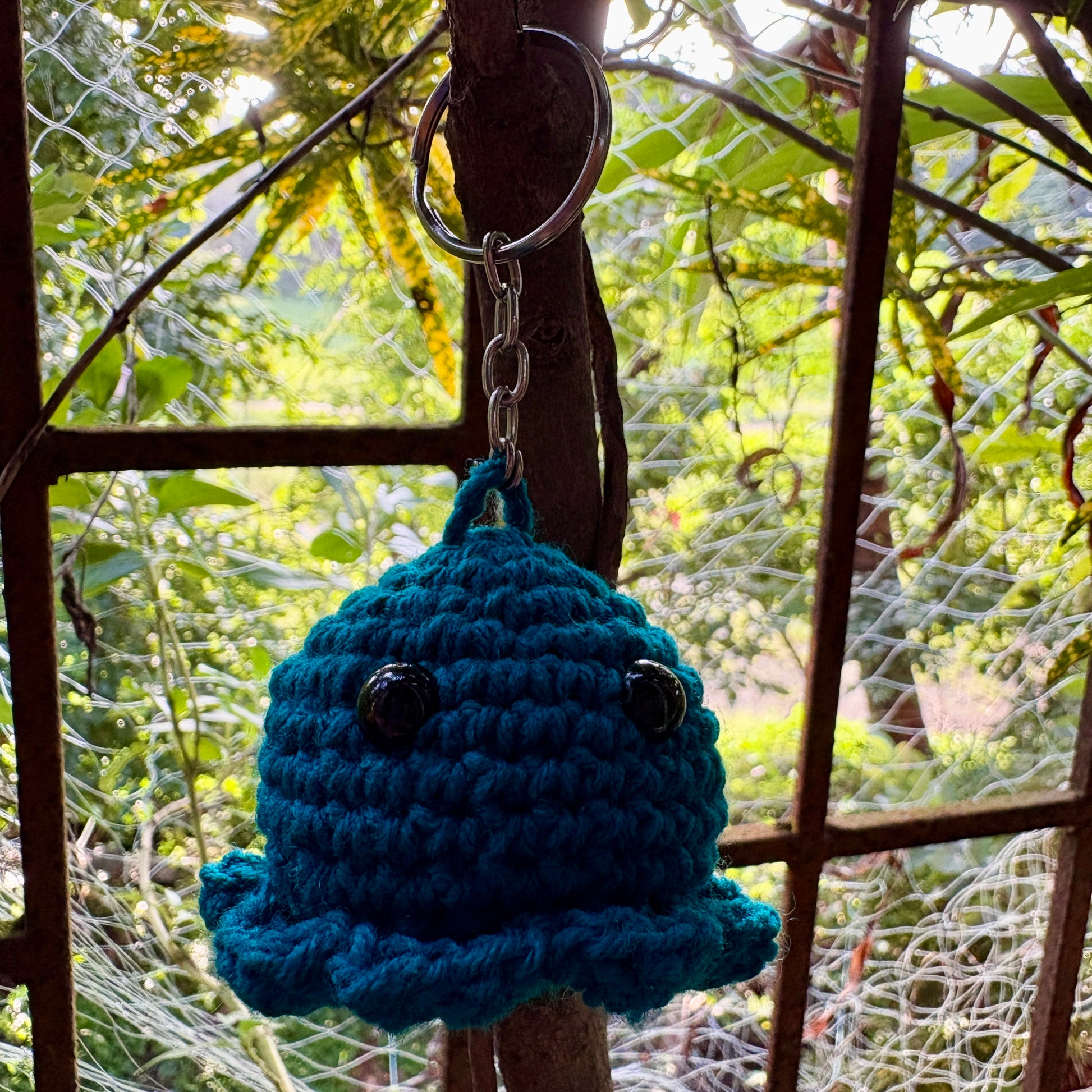 Blue crocheted bell keychain hanging on a metal hook with a natural background
