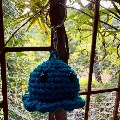 Blue crocheted bell keychain hanging on a metal hook with a natural background