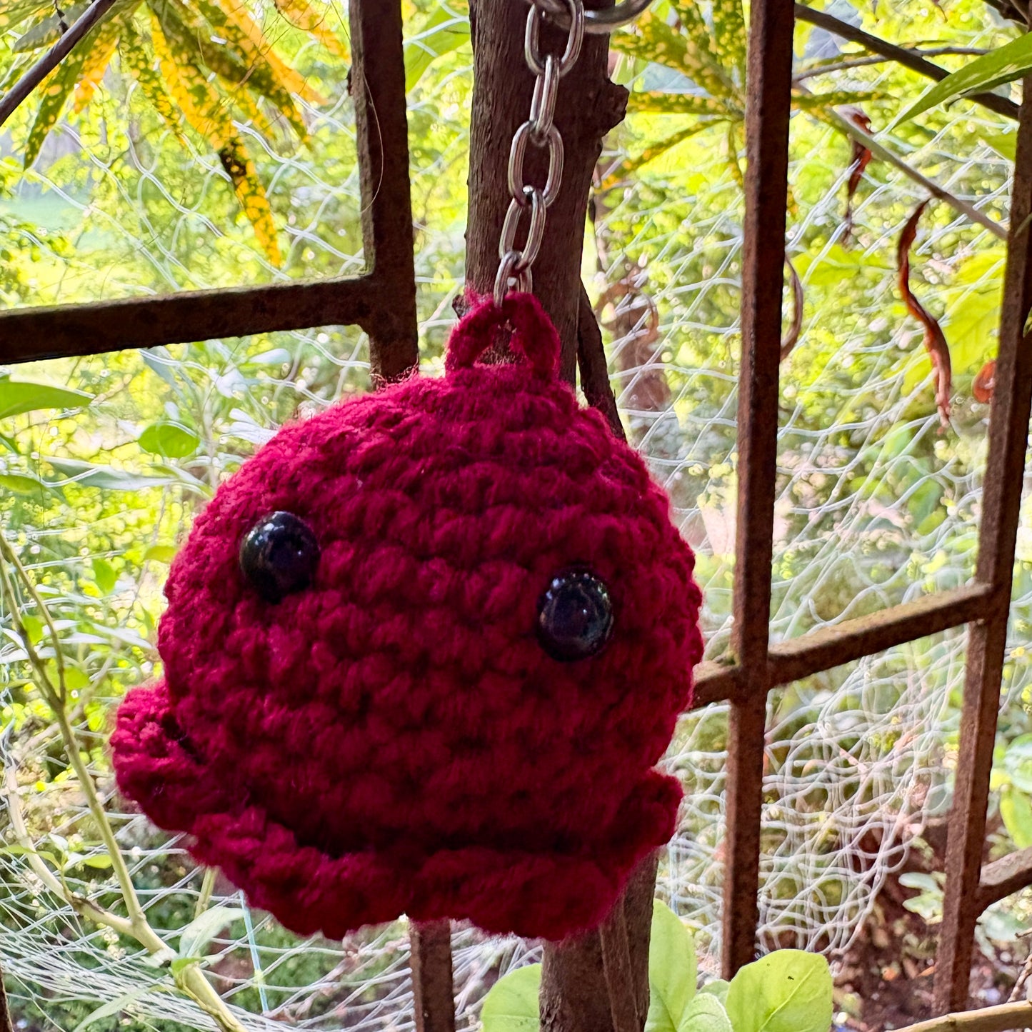 Crocheted keychain with a red ball and black eyes hanging from a chain against a natural background.
