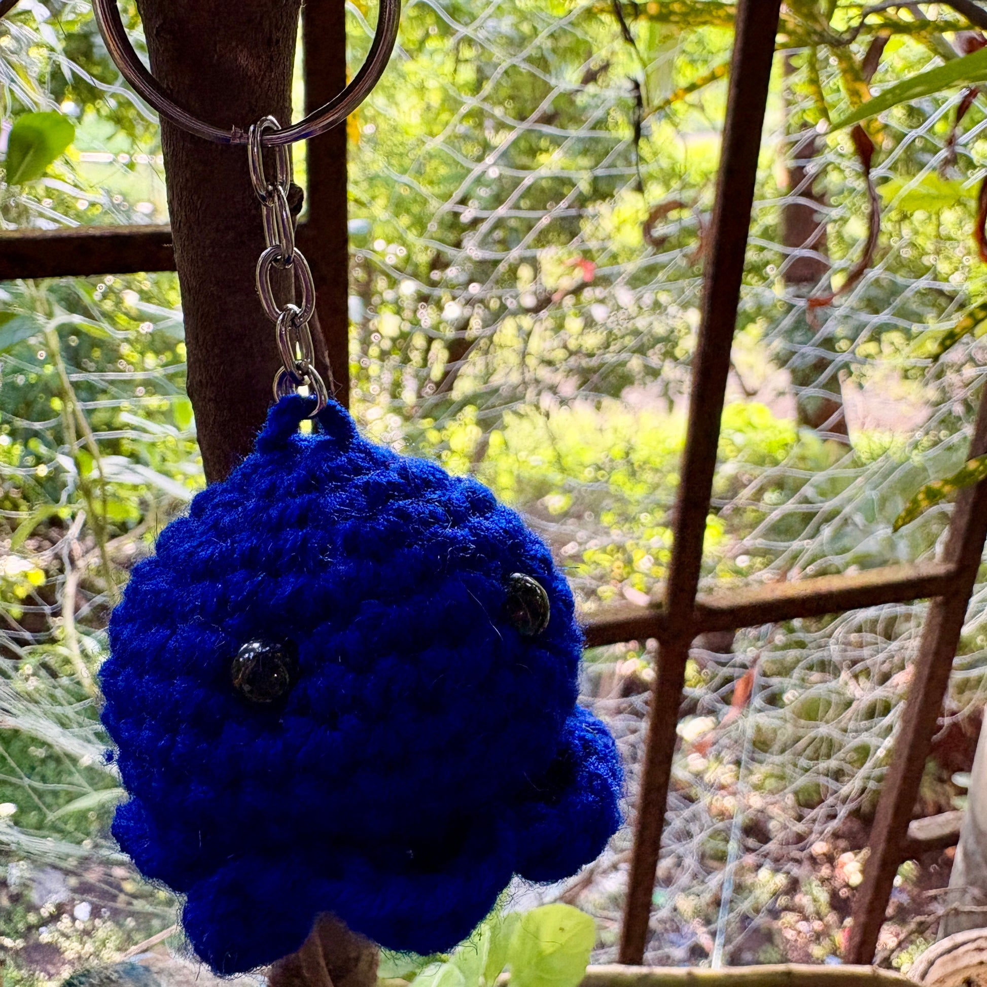 Blue crocheted keychain with a metal ring against a blurred natural background