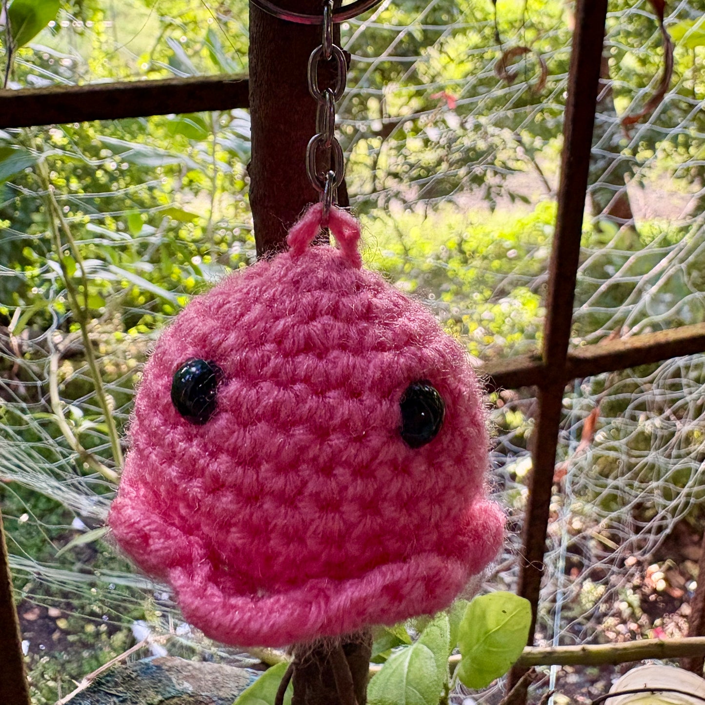 Pink crochet keychain with black eyes hanging on a branch with a natural background