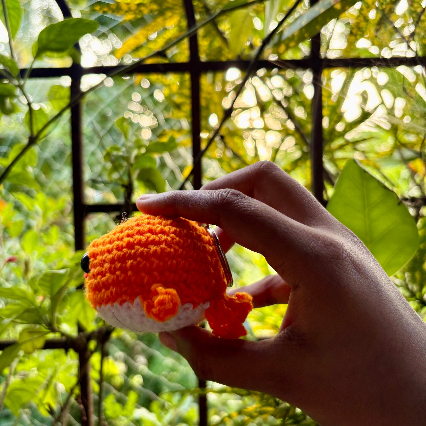 Hand holding a small crocheted whale against a green leafy background