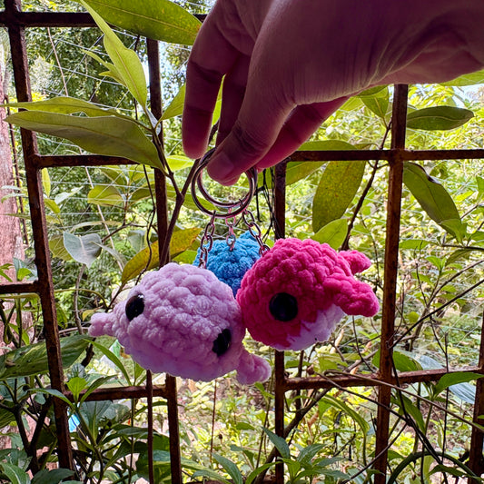 Three colorful plush keychains held by a hand against a natural background with greenery.