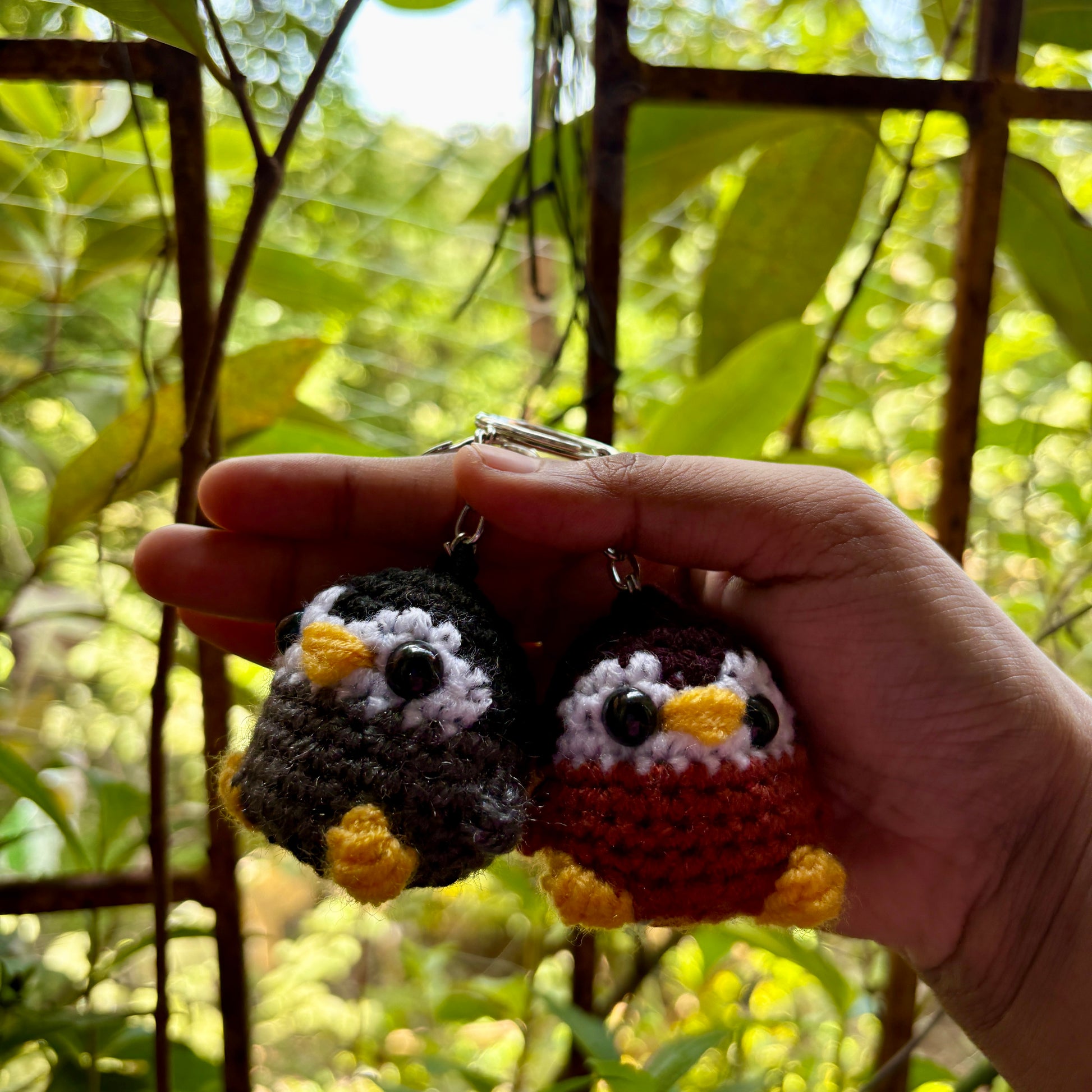 Hand holding two small crocheted penguin keychains with a natural background