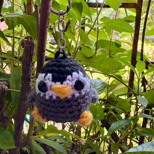 Crocheted penguin keychain hanging from a branch with green leaves in the background