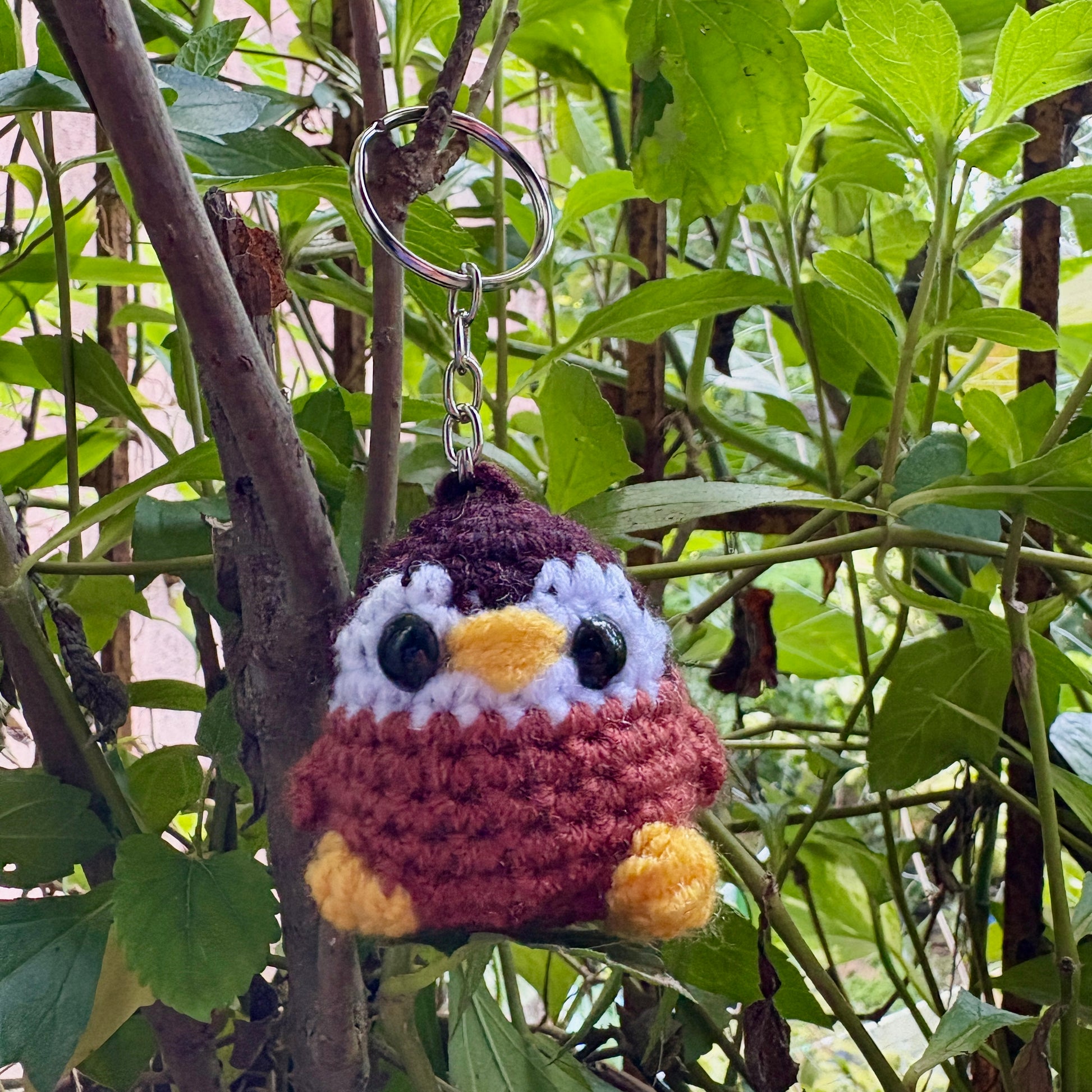 Crocheted bird keychain hanging from a branch with green leaves in the background