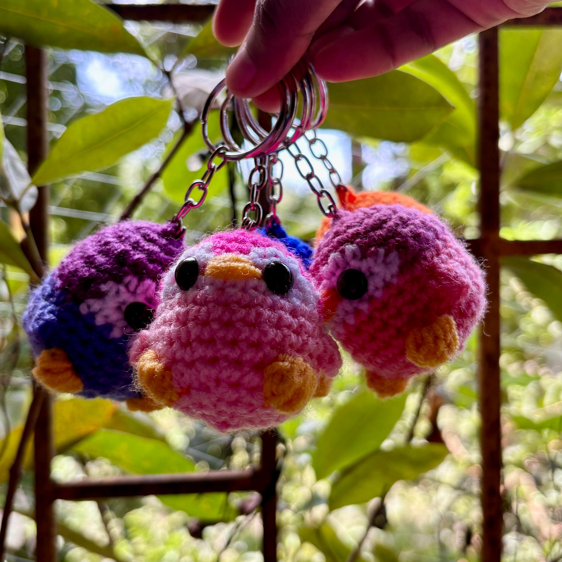 Colorful crocheted bird keychains hanging from a keychain holder against a natural background.