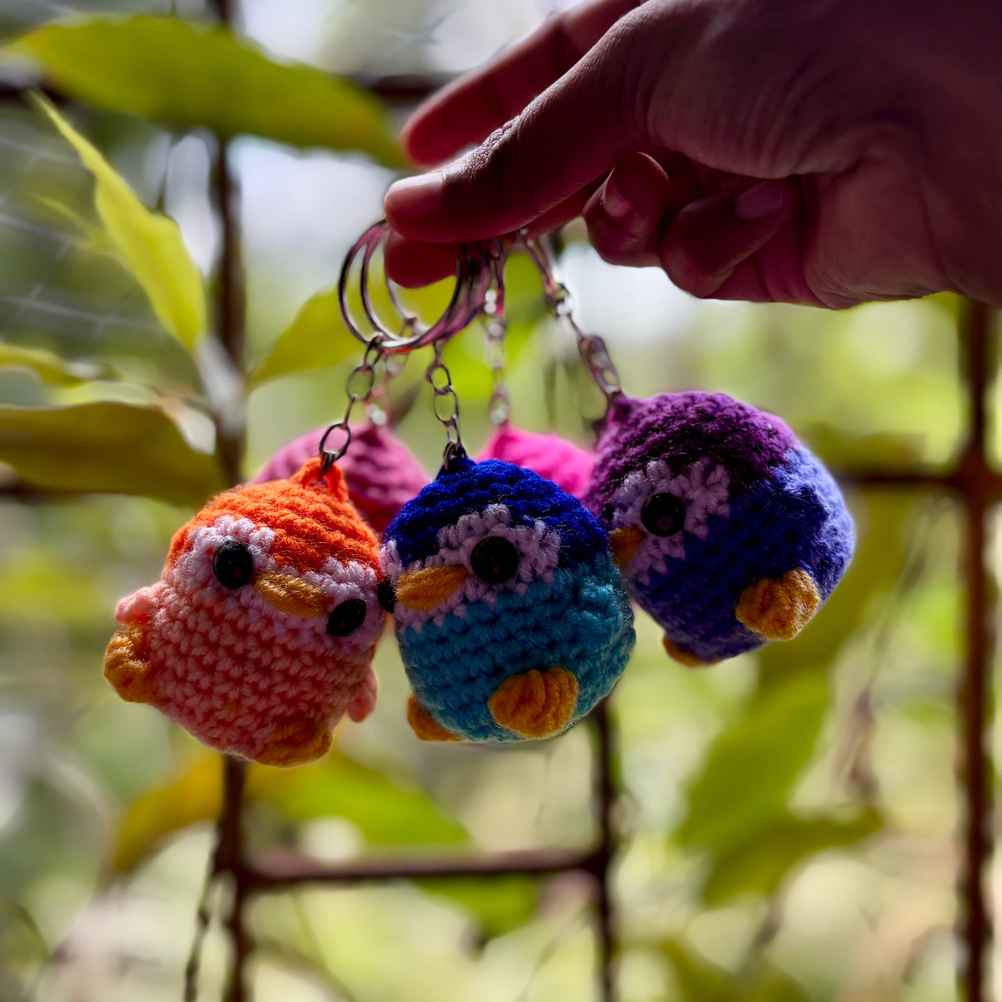 Colorful crocheted bird keychains held by a hand with a natural background