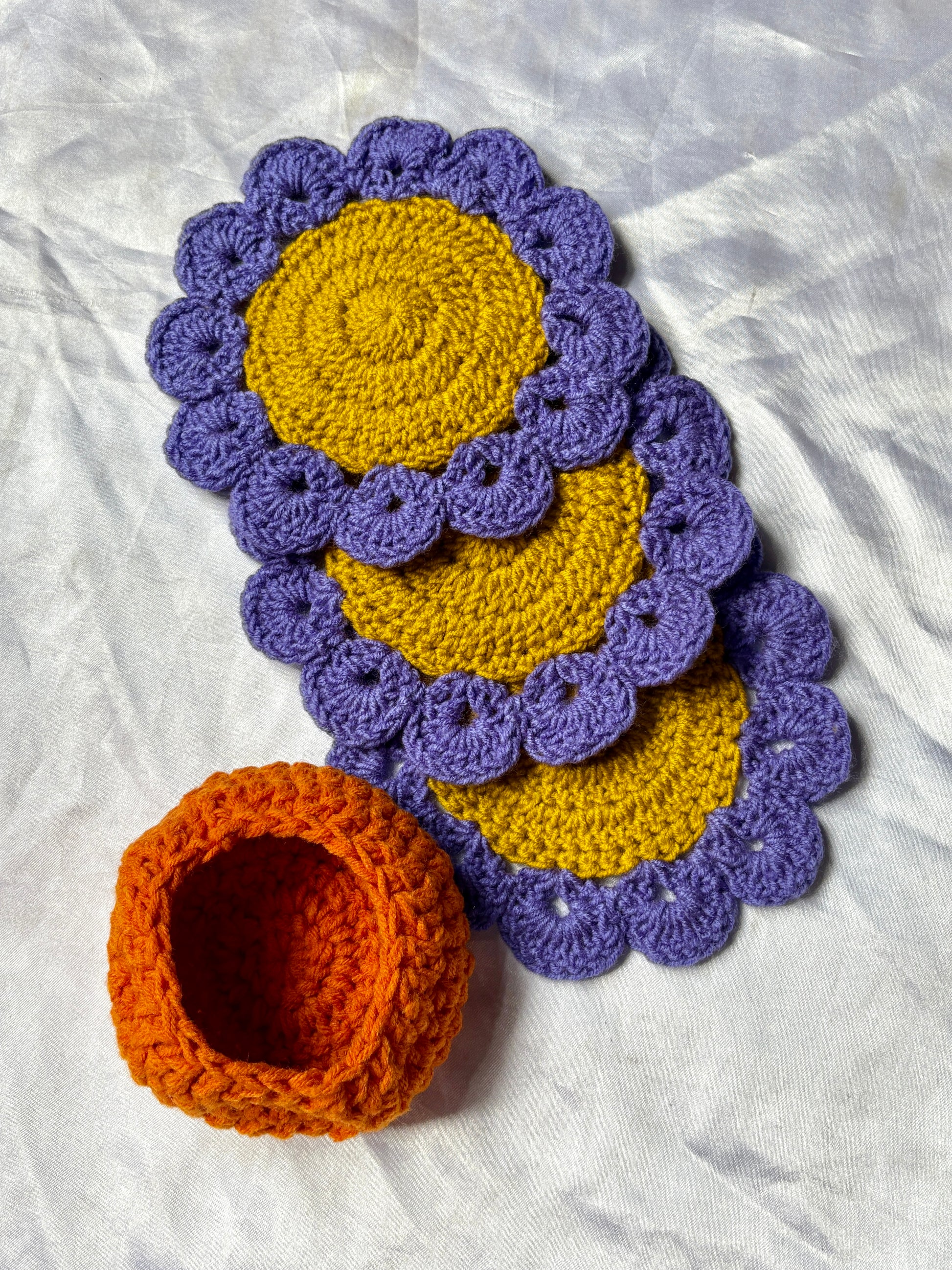 Crocheted coasters with purple scalloped edges and yellow centers on a white fabric background.