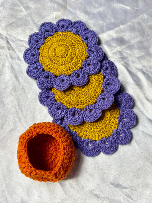 Crocheted coasters with purple scalloped edges and yellow centers on a white fabric background.