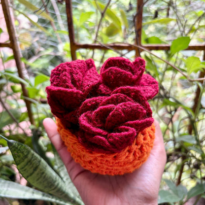 Hand holding a red and orange crochet flower coaster with pot against a natural background