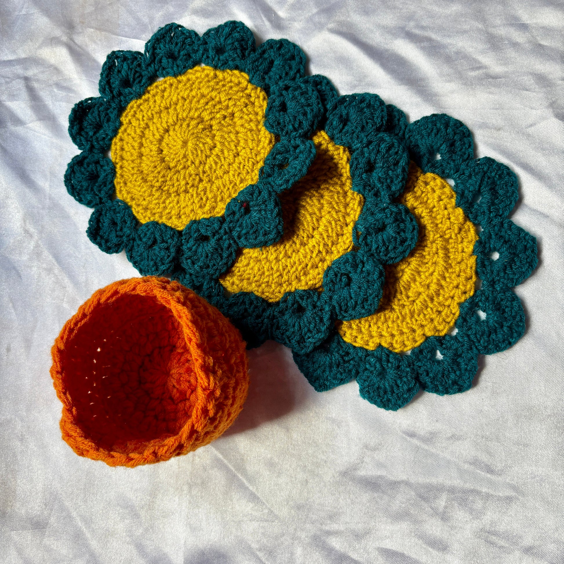 Crocheted coasters with yellow centers and teal borders on a white fabric background