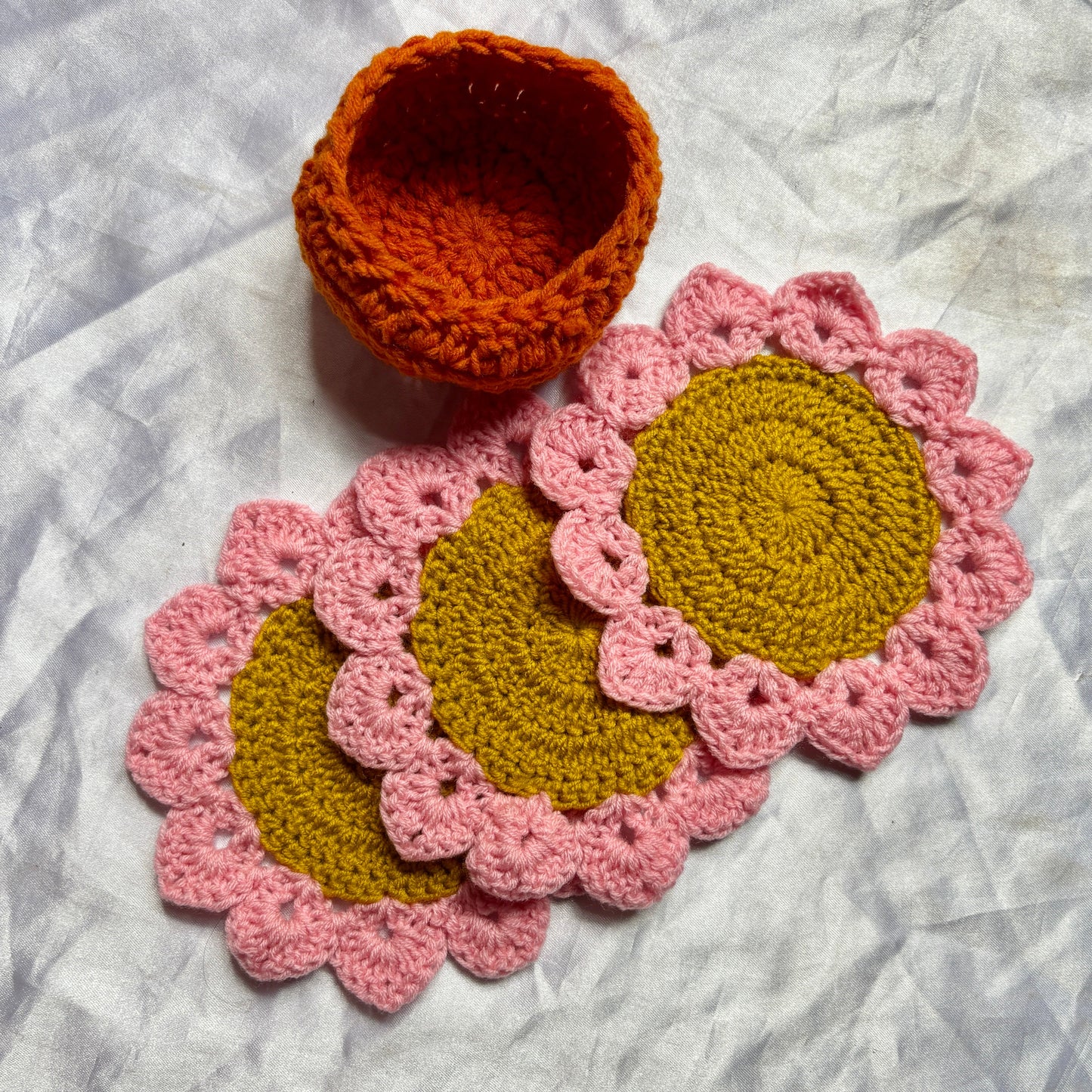 Set of crocheted coasters with pink rims and gold centers on a textured surface