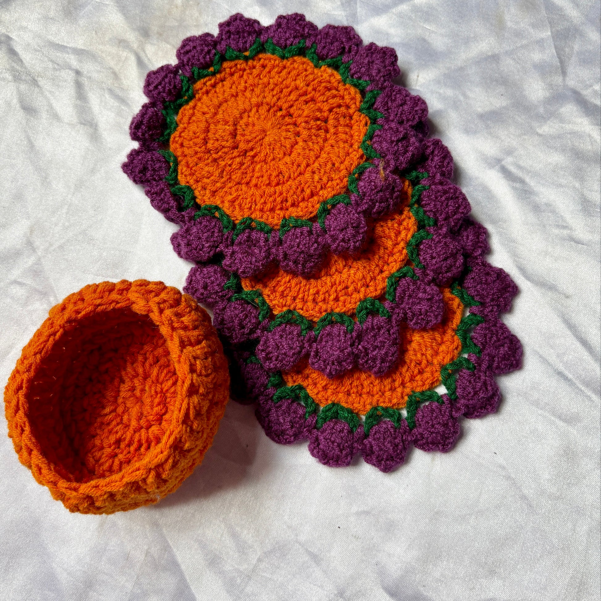 Set of purple and orange crocheted coasters on a white surface