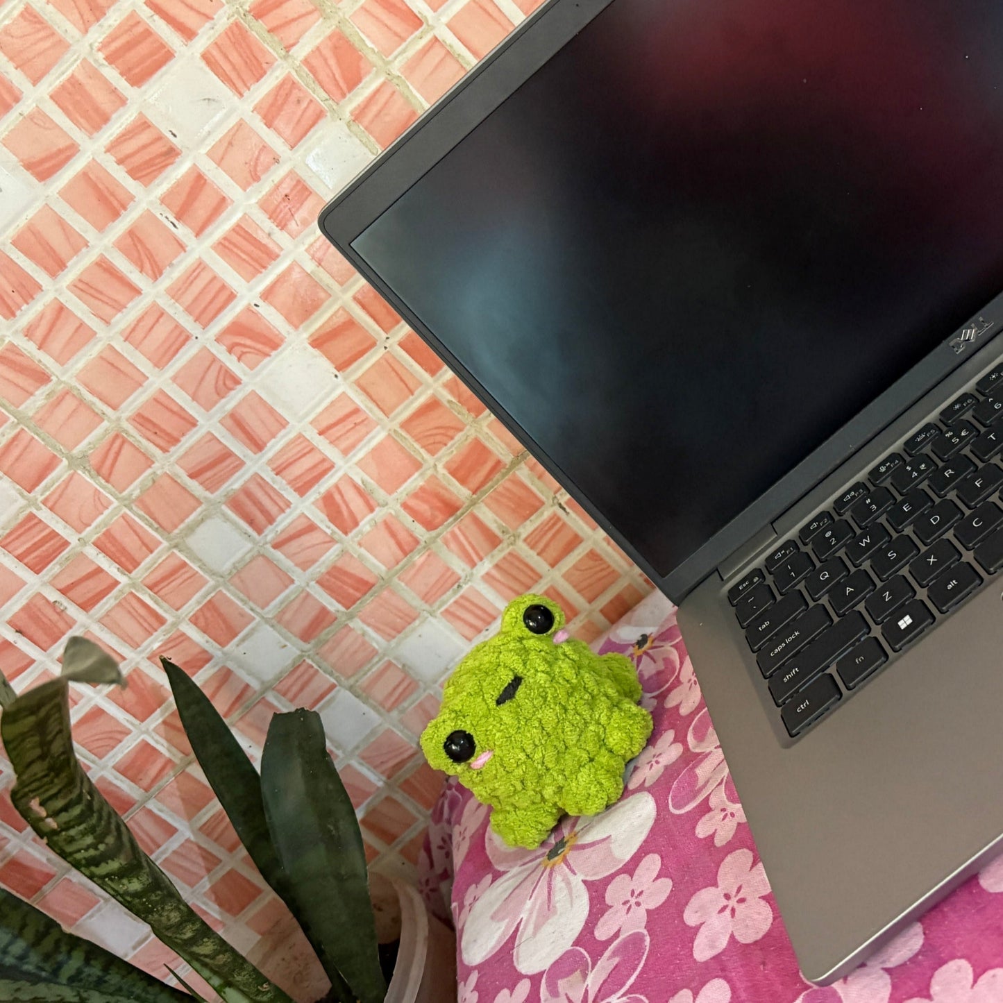 Laptop on a floral surface with a green plush toy next to it
