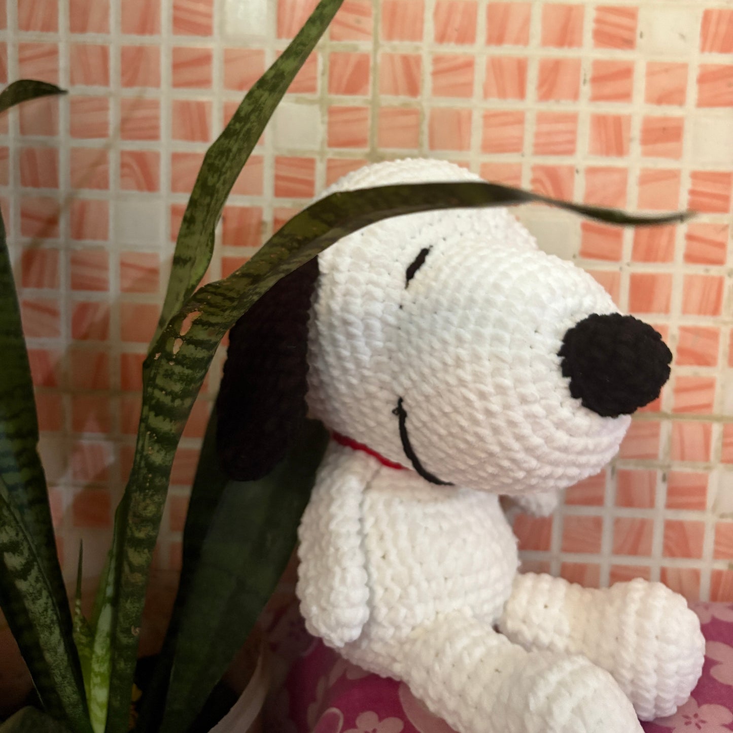 Crocheted dog toy with a black nose on a pink tiled wall background