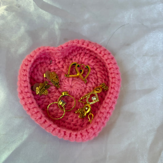 Pink heart-shaped crochet container with gold earrings on a white fabric background